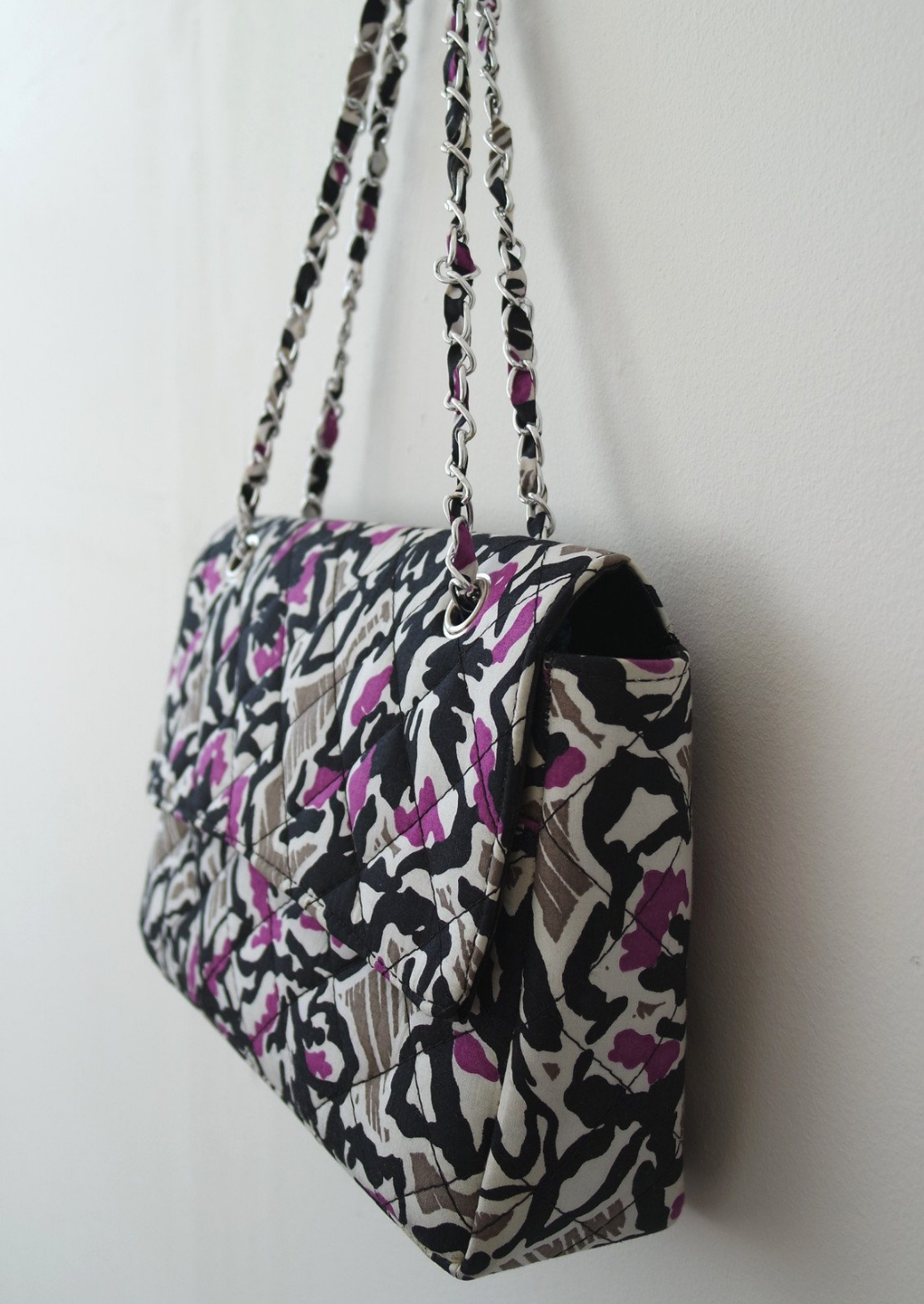 An Ankara African print handbag in hues of grey, purple and black. The bag has a chain handle detailing and fold over flap.