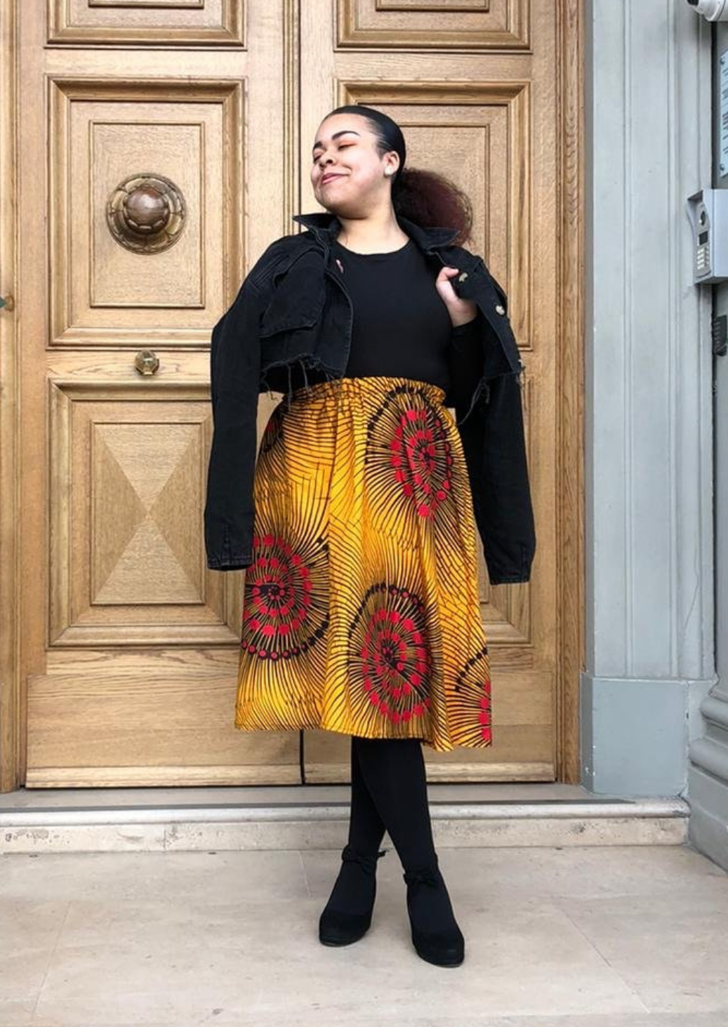 A yellow midi skirt, the pleated midi skirt is made from African print material, with pops of red and black scattered across the fabric.