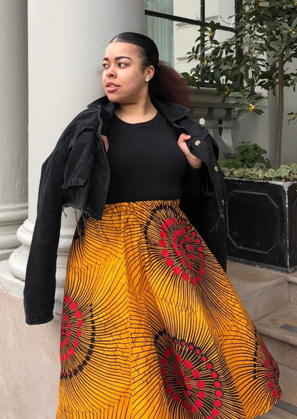 A yellow midi skirt, the pleated midi skirt is made from African print material, with pops of red and black scattered across the fabric.